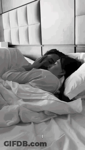 A Man And A Woman Are Laying In Bed Kissing . GIF