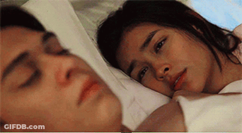 A Man And A Woman Are Laying In Bed Together And The Woman Is Looking At The Man . GIF