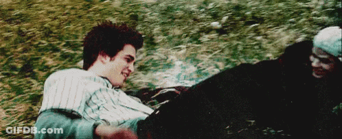 A Man And A Woman Are Laying In The Grass And Smiling At Each Other . GIF