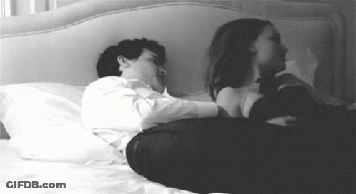 A Man And A Woman Are Laying On A Bed And Hugging Each Other . GIF