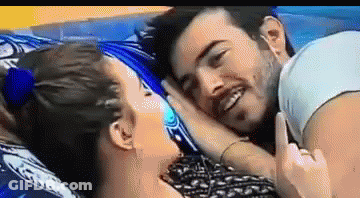 A Man And A Woman Are Laying On A Bed And The Woman Is Pointing At The Man 'S Face . GIF