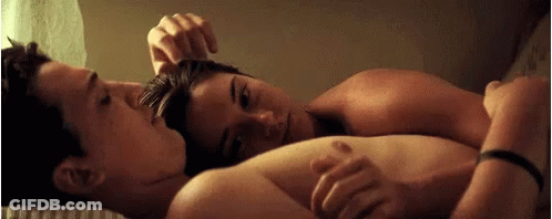 A Man And A Woman Are Laying On A Bed , The Woman Is Touching The Man 'S Hair . GIF