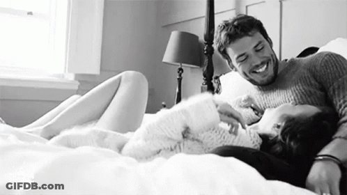 A Man And A Woman Are Laying On A Bed Together And Smiling . GIF