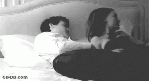 A Man And A Woman Are Laying On A Bed Together . GIF