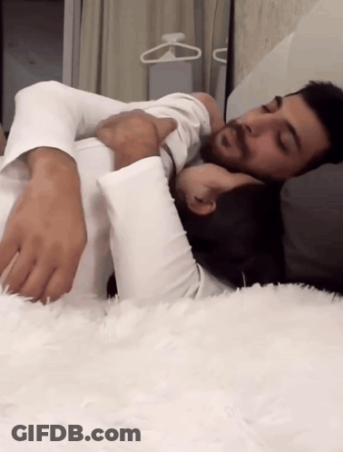 A Man And A Woman Are Laying On A Bed With Their Arms Around Each Other GIF