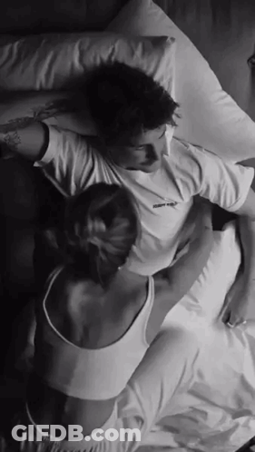 A Man And A Woman Are Laying On A Bed With Their Arms Around Each Other . GIF