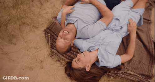 A Man And A Woman Are Laying On A Blanket In The Grass GIF