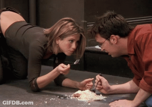 A Man And A Woman Are Looking At A Piece Of Food On The Floor GIF
