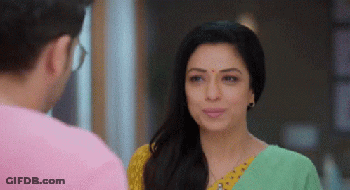 A Man And A Woman Are Looking At Each Other And Smiling . The Woman Is Wearing A Green And Yellow Sari . GIF