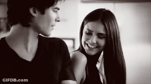A Man And A Woman Are Looking At Each Other And Smiling . GIF