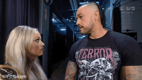 A Man And A Woman Are Looking At Each Other And The Man Is Wearing A Terror Shirt GIF