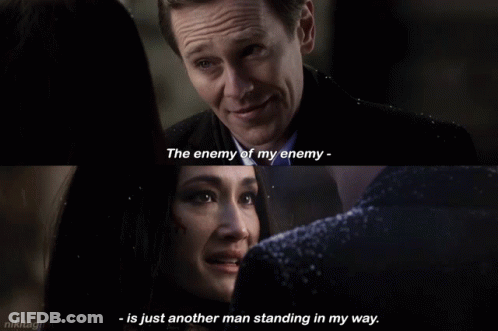 A Man And A Woman Are Looking At Each Other And The Man Says The Enemy Of My Enemy GIF