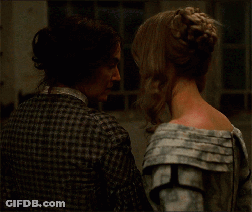 A Man And A Woman Are Looking At Each Other And The Woman Has A Bun In Her Hair GIF