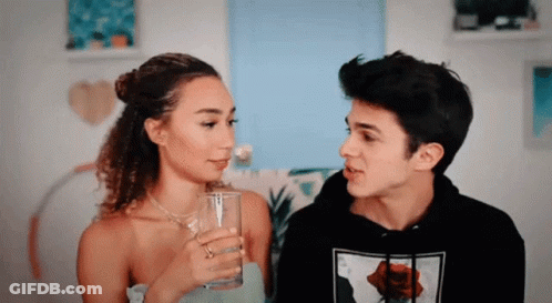 A Man And A Woman Are Looking At Each Other And The Woman Is Holding A Glass . GIF
