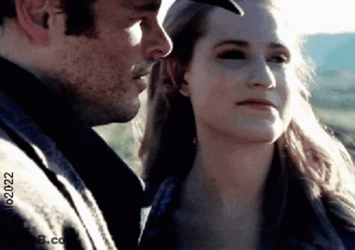 A Man And A Woman Are Looking At Each Other And The Woman Is Wearing A Hat . GIF