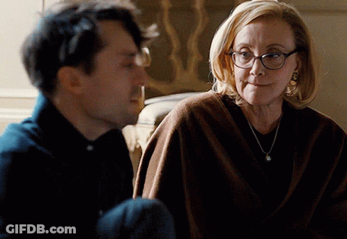 A Man And A Woman Are Looking At Each Other And The Woman Is Wearing Glasses GIF