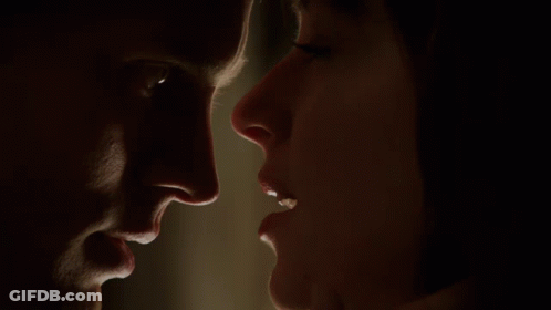 A Man And A Woman Are Looking At Each Other In A Dark Room GIF