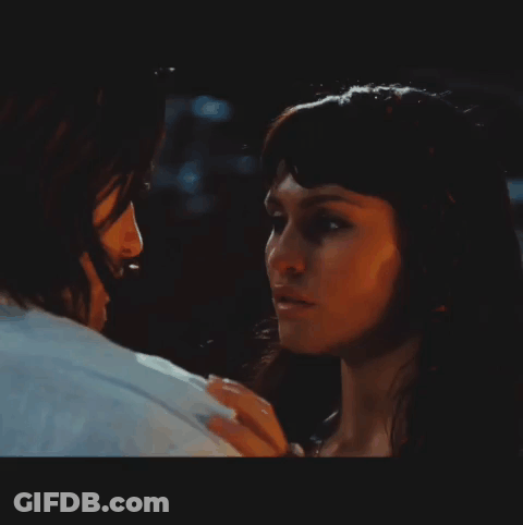 A Man And A Woman Are Looking At Each Other In A Dark Room GIF