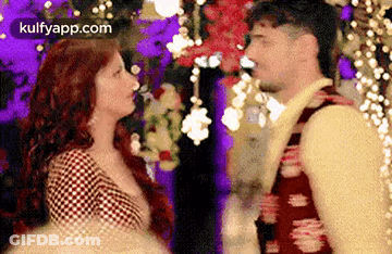 A Man And A Woman Are Looking At Each Other In A Room With Flowers In The Background . GIF