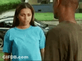 A Man And A Woman Are Looking At Each Other In Front Of A Car . GIF