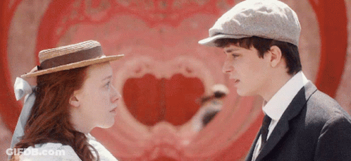 A Man And A Woman Are Looking At Each Other In Front Of A Heart Shaped Wall GIF