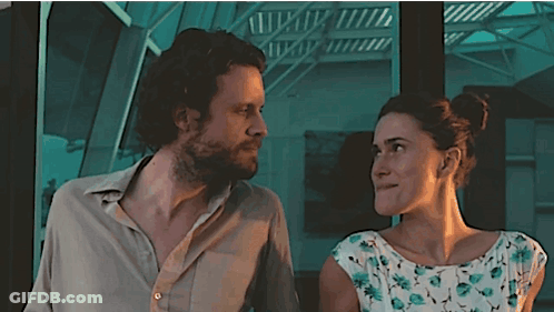 A Man And A Woman Are Looking At Each Other In Front Of A Staircase GIF