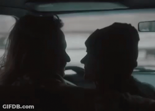 A Man And A Woman Are Looking At Each Other In The Back Seat Of A Car . GIF