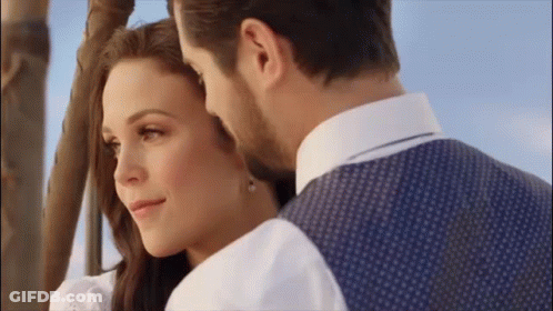 A Man And A Woman Are Looking At Each Other While Standing Next To A Hot Air Balloon . GIF