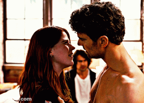A Man And A Woman Are Looking At Each Other With A Man In The Background GIF
