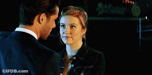 A Man And A Woman Are Looking At Each Other With A Sign In The Background That Says Mccafe GIF