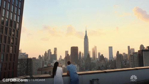 A Man And A Woman Are Looking At The City Skyline And The Empire State Building GIF
