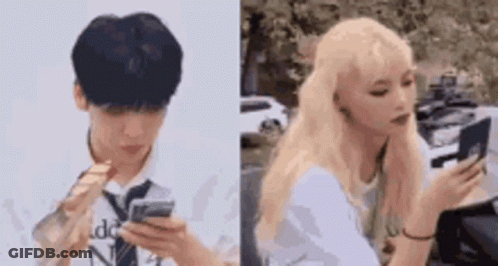 A Man And A Woman Are Looking At Their Phones . The Man Is Wearing A Tie And The Woman Is Blonde . GIF