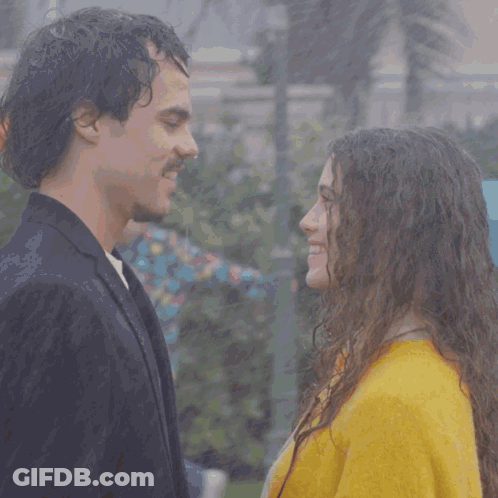 A Man And A Woman Are Looking Into Each Other 'S Eyes And The Woman Is Wearing A Yellow Sweater GIF