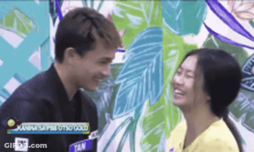 A Man And A Woman Are Looking Into Each Other 'S Eyes In Front Of A Mural . GIF