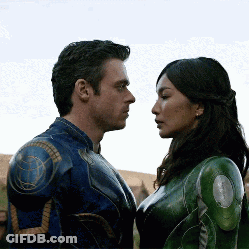A Man And A Woman Are Looking Into Each Other 'S Eyes . The Woman Is Wearing A Green Suit . GIF