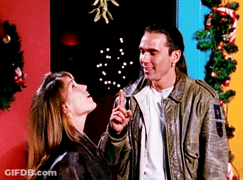 A Man And A Woman Are Looking Up At A Mistletoe GIF