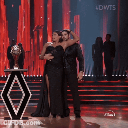 A Man And A Woman Are On A Stage With A Trophy In The Background And The Words #Dwts On The Bottom GIF