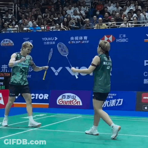 A Man And A Woman Are Playing Badminton On A Court With Advertisements For Ganten And Hsbc GIF
