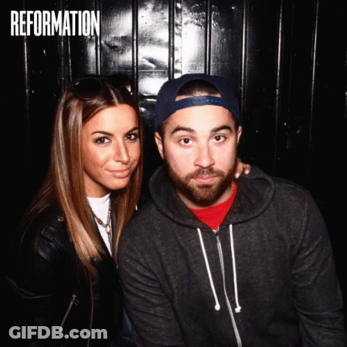 A Man And A Woman Are Posing For A Photo In Front Of A Wall That Says " Reformation " GIF