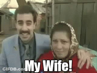 A Man And A Woman Are Posing For A Picture And The Woman Is Wearing A Scarf And The Man Is Smiling . GIF