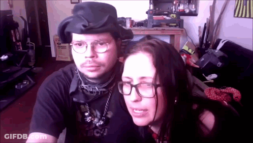 A Man And A Woman Are Posing For A Picture And The Woman Is Wearing Glasses And A Black Shirt That Says Bcj GIF