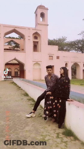 A Man And A Woman Are Posing For A Picture In Front Of A Pink Building With Tiktok Written On The Bottom GIF