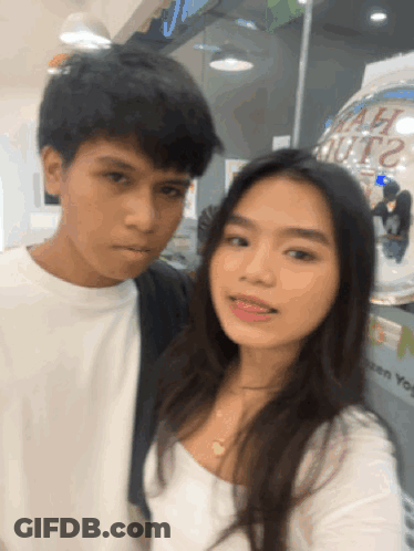 A Man And A Woman Are Posing For A Picture In Front Of A Sign That Says " Chicken You " GIF
