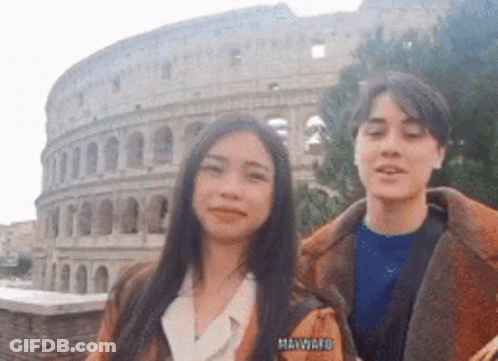 A Man And A Woman Are Posing For A Picture In Front Of The Colosseum In Rome . GIF