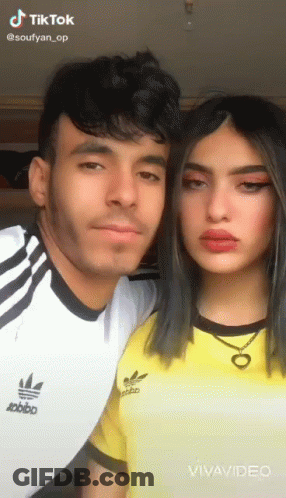 A Man And A Woman Are Posing For A Picture . The Woman Is Wearing A Yellow Adidas Shirt . GIF