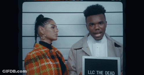 A Man And A Woman Are Posing For A Picture With A Sign That Says Llc The Dead GIF