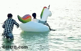 A Man And A Woman Are Riding On A Unicorn Float In The Water . GIF