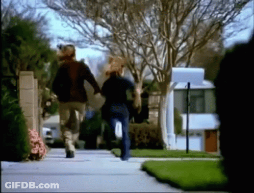 A Man And A Woman Are Running Down A Street Holding Hands . GIF