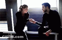 A Man And A Woman Are Shaking Hands While Sitting On A Bench In Front Of A Window . GIF