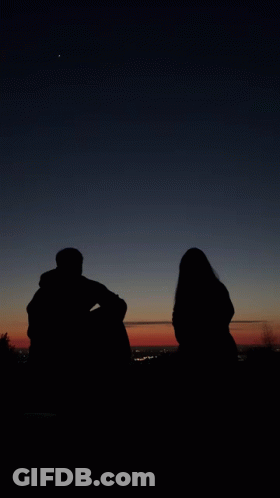 A Man And A Woman Are Silhouetted Against A Dark Sky GIF